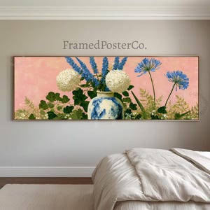Könnte beinhalten: Ein Panorama-Wandkunstdruck mit einer blau-weißen Keramikvase, gefüllt mit weißen Hortensien und hohen blauen Ritterspornstielen vor einem zartrosa Hintergrund. Der Text FramedPosterCo. ist über dem Blumenarrangement zu sehen.