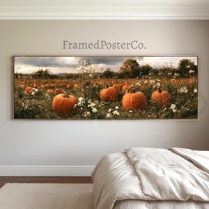 以下が含まれることがあります： FramedPosterCo.というタイトルのパノラマウォールアートプリント。曇り空の下、緑の草と白い野草の中にオレンジ色のカボチャが点在するカボチャ畑の風景が描かれており、白い掛け布団の白いベッドの上に飾られています。