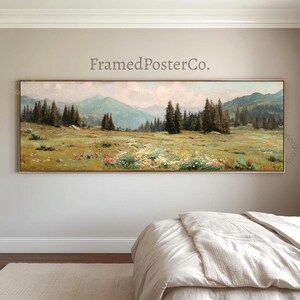 Puede incluir: Una pintura de paisaje enmarcada que representa un prado con flores silvestres, árboles de hoja perenne y montañas al fondo. La obra de arte tiene un marco dorado, con el texto "FramedPosterCo." visible en la parte superior.