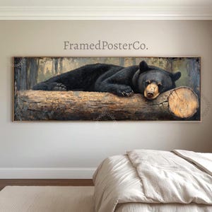May include: A panoramic framed wall art print featuring a black bear resting on a large, textured wooden log. The bear has dark fur and is positioned horizontally across the log. The background depicts a forest setting. The text FramedPosterCo. is visible.