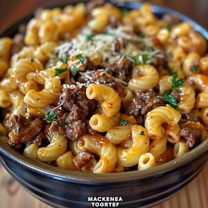 Könnte beinhalten: Nahaufnahme einer Schüssel mit Makkaroni und Rindfleisch. Die Nudeln sind in einer reichhaltigen, orangefarbenen Sauce bedeckt und mit geriebenem Käse und frischer Petersilie garniert. Das Rindfleisch ist in kleinen, gebräunten Stücken. Die Schüssel hat unten den Text "MACKENEA TOGRTEF".