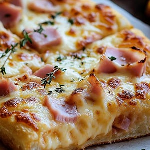 Puede incluir: Primer plano de una porción de pizza rectangular con queso derretido, jamón y hierbas. La corteza es dorada y el queso está burbujeante y ligeramente dorado. El jamón es rosado y está distribuido uniformemente.