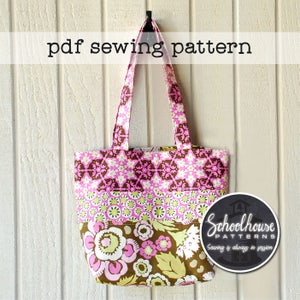 Op de afbeelding: Een roze en bruine draagtas met een bloemenpatroon. De tas heeft één handvat en hangt aan een witte muur. De tekst "pdf sewing pattern" staat bovenaan de afbeelding. De tekst "Schoolhouse Patterns" staat onderaan de afbeelding. De tekst "Sewing is always in session" staat onder het logo.