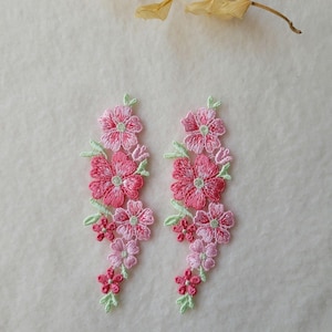 以下が含まれることがあります： 2つの刺繍された花のアップリケ。各アップリケは、緑の葉と茎を持つピンクの花のクラスターを特徴としています。花は、淡いピンクから濃いバラ色まで、繊細で詳細なデザインを作り出しています。