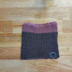 May include: A two-toned knitted hat with a pink top and a dark gray bottom. The hat has a small sheep logo attached to the side.