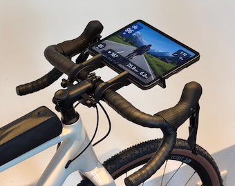 May include: A white bicycle handlebar assembly featuring a black tablet mount holding a tablet displaying cycling metrics and a virtual road scene. The handlebars are wrapped in black tape, and a black storage bag is attached to the frame.