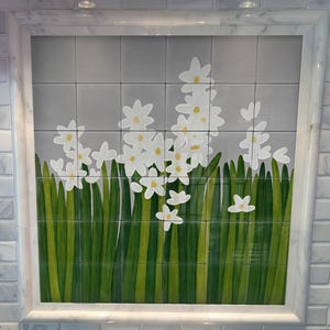 May include: A contemporary kitchen featuring a stainless steel gas hob and a decorative backsplash. The backsplash showcases a floral design of white flowers and green stems on a grey tile background. The hob has black grates and a digital display.