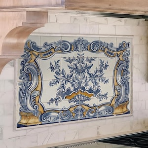 May include: A kitchen range hood with a light wood trim and a white metal top. The backsplash features decorative tiles with blue and yellow floral patterns. The kitchen also includes a stainless steel range and a marble countertop.