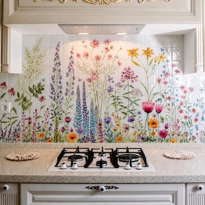May include: A kitchen backsplash featuring a grid of white ceramic tiles printed with a colorful botanical illustration of various wildflowers, including tall purple, pink, yellow, and orange blossoms, positioned above a white gas stovetop.