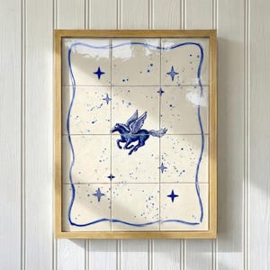 May include: A framed artwork featuring a Pegasus illustration. The artwork is composed of nine square tiles with a cream background. The Pegasus is depicted in blue, surrounded by blue stars and splatters. The frame is made of light-colored wood.