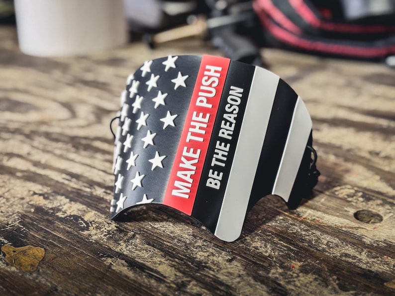 May include: A curved black, white, and red accessory featuring a stylized American flag design with white stars on the left and horizontal stripes on the right. The text "MAKE THE PUSH" and "BE THE REASON" is printed in white on the red and black sections.