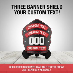May include: Black and red firefighter helmet shield with the text "THREE BANNER SHIELD YOUR CUSTOM TEXT!". The shield has three red banners with the text "CUSTOM TEXT" and the number "000".