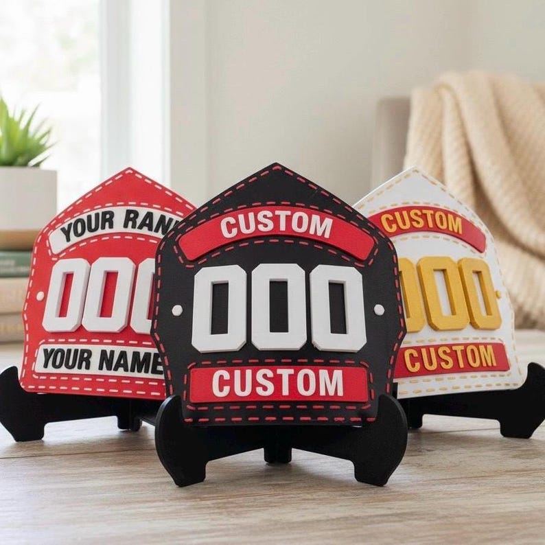 3D Printed Firefighter Helmet Shields displayed on black stands. The image shows three PLA replica shields: one black, one red, and one white/yellow, each featuring customizable text areas for name, rank, and number. This photo highlights the personalized fireman plaque and custom firehouse decor options, making it an ideal firefighter gift for graduation or retirement.