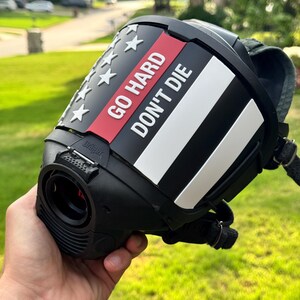 May include: A black protective face mask featuring a custom overlay with a stylized American flag design. The overlay includes white stars, a thin red stripe, and the white text GO HARD DON'T DIE printed on the front. The mask has a black frame.