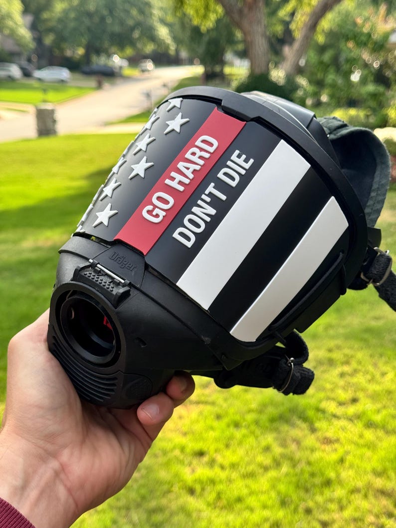 May include: A black protective face mask featuring a custom overlay with a stylized American flag design. The overlay includes white stars, a thin red stripe, and the white text GO HARD DON'T DIE printed on the front. The mask has a black frame.