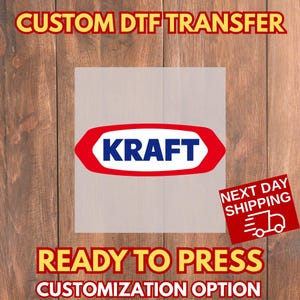 May include: A custom DTF transfer featuring the Kraft logo in a red and white design. The text "READY TO PRESS" and "CUSTOMIZATION OPTION" are displayed in yellow. The background is a wood grain pattern.