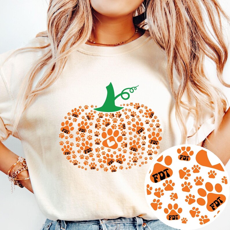 Puede incluir: Sudadera color crema con un dise&ntilde;o de calabaza hecho de huellas de patas naranjas. La calabaza tiene un tallo verde y una huella de pata en forma de coraz&oacute;n en el centro. Las letras "FDT" est&aacute;n impresas en algunas huellas.
