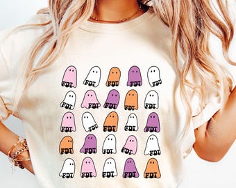 May include: Cream-colored t-shirt featuring a grid of cartoon ghosts in various colors, including pink, orange, purple, and white. Each ghost has the letters "FDT" printed on it. The shirt is a casual, everyday wear item.