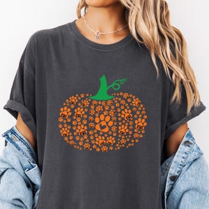 Puede incluir: Camiseta gris oscuro con un dise&ntilde;o de calabaza hecho de huellas de patas naranjas y las letras "FDT". La calabaza tiene un tallo verde y est&aacute; centrada en la camiseta. Un coraz&oacute;n est&aacute; dentro de una de las huellas.