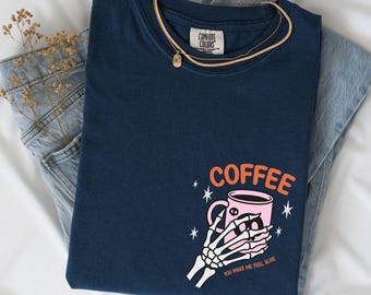 May include: Navy blue Comfort Colors sweatshirt with a graphic of a skeleton hand holding a pink coffee mug. The word "COFFEE" is above the mug in orange, and the text "YOU MAKE ME FEEL ALIVE" is below. A gold necklace and blue jeans are also in the image.