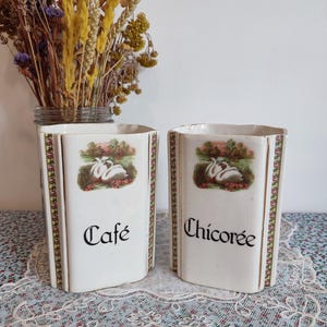 Puede incluir: Dos botes de cerámica blanca con ribetes dorados e ilustraciones de cisnes. Los botes están etiquetados como "Cafe" y "Chicoree".