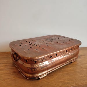 Peut inclure: Un chauffe-plat rectangulaire en cuivre avec un couvercle perforé et des côtés martelés. Le chauffe-plat antique a une poignée sur un côté et repose sur de petits pieds. Le cuivre a une teinte brun-rougeâtre chaude.