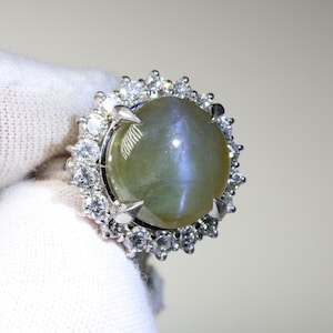 May include: A silver ring featuring a large, round, green gemstone encircled by smaller, clear gemstones.