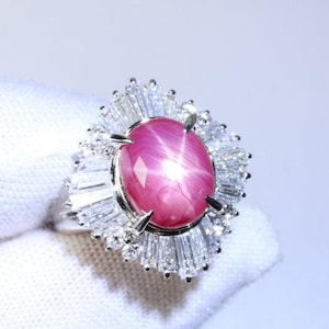 May include: A pink star ruby ring set in white gold with a halo of baguette-cut diamonds.