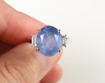Könnte beinhalten: Silberring mit einem großen, oval geschliffenen, hellblauen Edelstein, flankiert von zwei kleineren, rechteckigen, klaren Edelsteinen. Der Ring vor weißem Hintergrund.