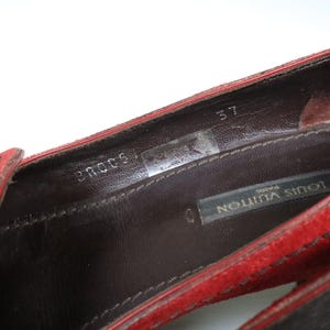 May include: Close-up of a red suede shoe interior. The shoe features a dark brown leather insole with the brand name "LOUIS VUITTON PARIS" visible. The size is marked as "37".
