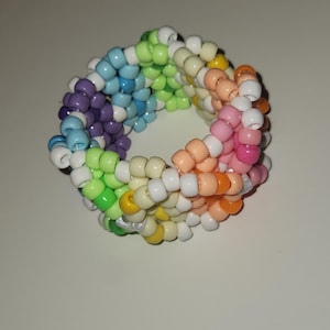 Puede incluir: Una pulsera de cuentas multicolores. La pulsera está hecha de pequeñas cuentas redondas de varios colores, incluyendo morado, azul, verde, amarillo, naranja, rosa y blanco. Las cuentas están ensartadas para formar una forma circular.