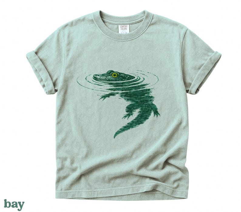 Bay Comfort Colors shirt featuring a vintage-style green alligator partially submerged in water with circular ripples and a bright yellow-green eye.