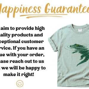 May include: A pale green t-shirt with a green alligator design. The text reads "Happiness Guarantee" and a customer service statement. The shirt is a casual wear item. The image also contains a smiling face.