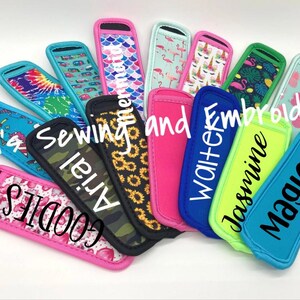 Puede incluir: Una colecci&oacute;n de coloridas fundas para bebidas de neopreno con varios dise&ntilde;os y textos. Los dise&ntilde;os incluyen tie-dye, flamencos y pi&ntilde;as. Algunas fundas tienen nombres como "Arial" y "Jasmine". Tambi&eacute;n se ve el texto "Tini's Sewing and Embroidery".