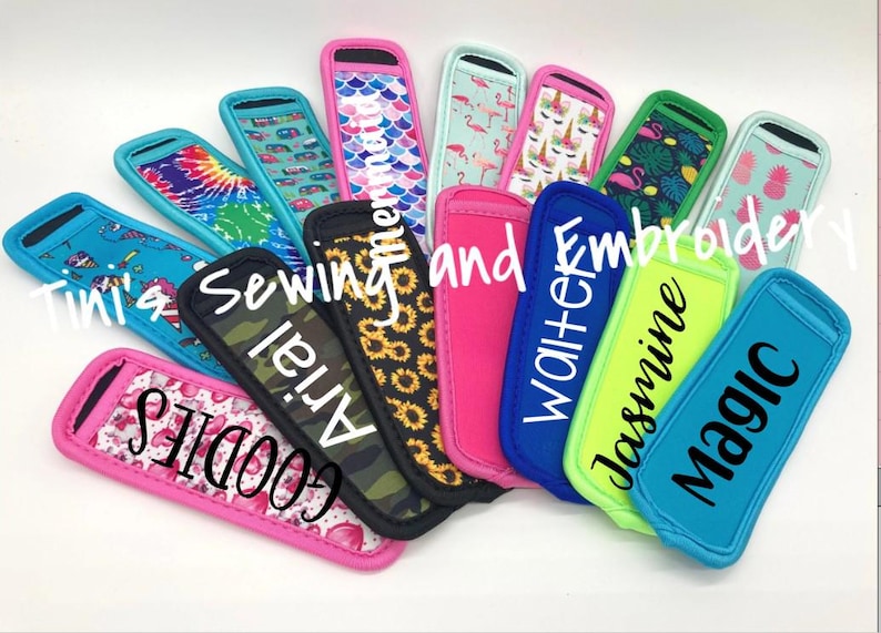 Puede incluir: Una colecci&oacute;n de coloridas fundas para bebidas de neopreno con varios dise&ntilde;os y textos. Los dise&ntilde;os incluyen tie-dye, flamencos y pi&ntilde;as. Algunas fundas tienen nombres como "Arial" y "Jasmine". Tambi&eacute;n se ve el texto "Tini's Sewing and Embroidery".