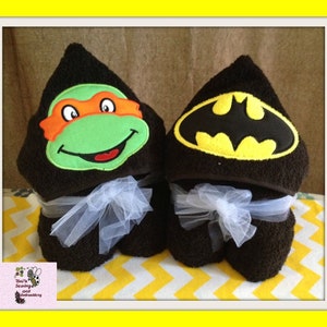 May include: Two hooded towels, one with a green and orange Teenage Mutant Ninja Turtles face and the other with a black and yellow Batman logo.