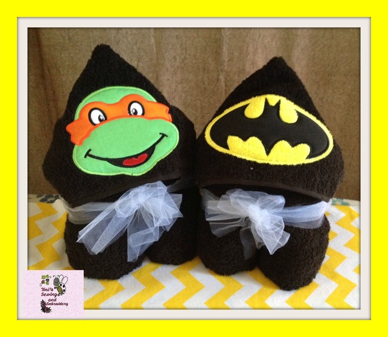 May include: Two hooded towels, one with a green and orange Teenage Mutant Ninja Turtles face and the other with a black and yellow Batman logo.