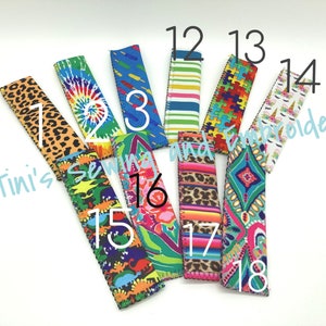 Puede incluir: Una colección de 18 enfriadores de latas coloridos con varios patrones, que incluyen tie-dye, estampado de animales y diseños geométricos. Los enfriadores están numerados del 12 al 18. El texto "Tini's Sewing and Embroidery" es visible en la esquina inferior izquierda.