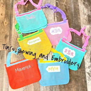 May include: Six colourful mesh bags with adjustable straps and zipper closures. Each bag has a personalised name embroidered on it: Shells, MYR, Benjamin, DBR, MYH, and Maverick.