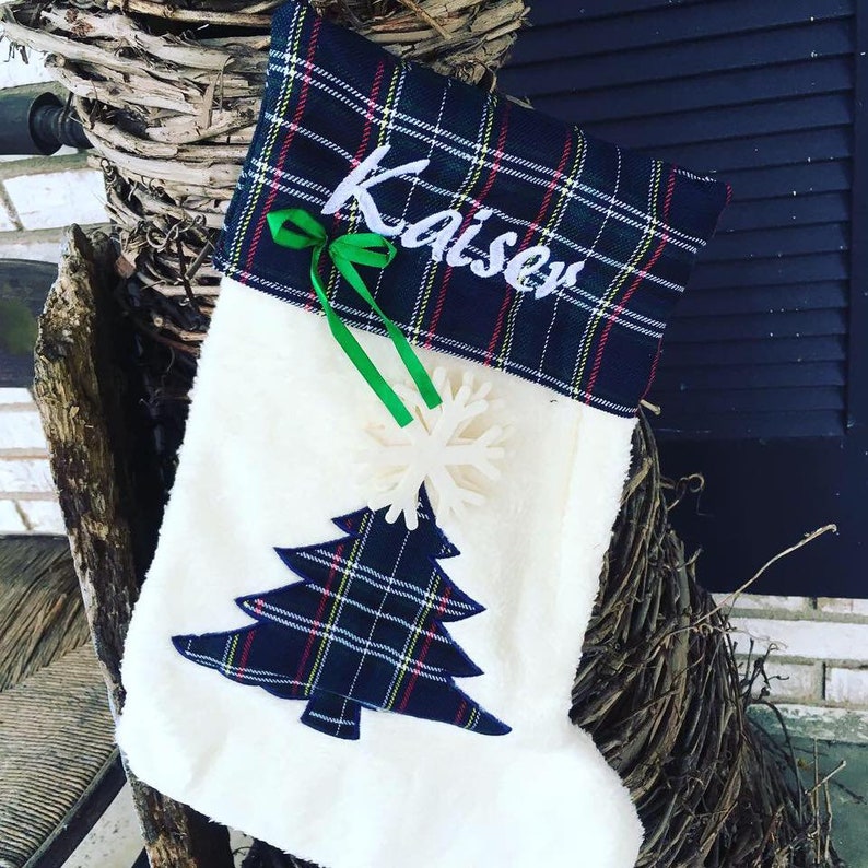 May include: White Christmas stocking with a blue and green plaid cuff. The cuff has the name "Kaiser" embroidered on it. The stocking has a blue and green plaid Christmas tree applique and a white snowflake.