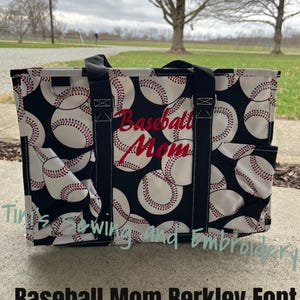 Peut inclure: Un sac fourre-tout noir avec un motif de balles de baseball blanches et des coutures rouges. Le sac a des poignées noires et les mots "Baseball Mom" brodés en rouge. Le sac a deux poches latérales.