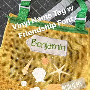 May include: A yellow mesh bag with a green zipper and green straps. The bag has a white vinyl name tag with the text "Benjamin" in a green font. The bag also has a white starfish and seashells printed on it. The text "#TINISSEWINGAN" and "Vinyl Name Tag w Friendship Font" are visible on the bag.