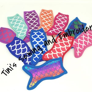 May include: A set of ten mermaid tail-shaped can coolers in various colors, including blue, pink, purple, orange, and green. The coolers are made of neoprene and feature a scale pattern. The text "Tini's Sewing and Embroidery" is visible in the image.