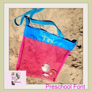 May include: A pink mesh beach bag with a blue top and strap, resting on sand. The name "Tini" is embroidered in yellow. The bag contains seashells. The text "Preschool Font" is at the bottom.