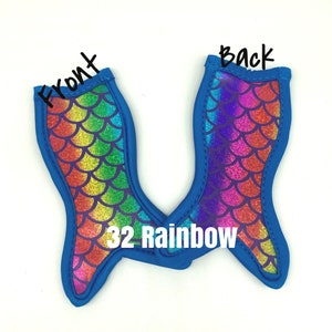 May include: Two blue mermaid tail shaped can coolers with a rainbow glitter pattern. The front of the cooler has a rainbow pattern and the back has a purple and pink pattern. The text "32 Rainbow" is printed on the cooler.