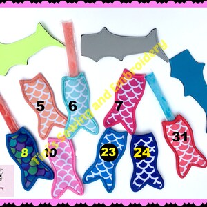 May include: Assortment of ten mermaid tail popsicle holders in various colors, including pink, blue, green, and orange. The holders are made of fabric with a scale pattern and have numbers on them.
