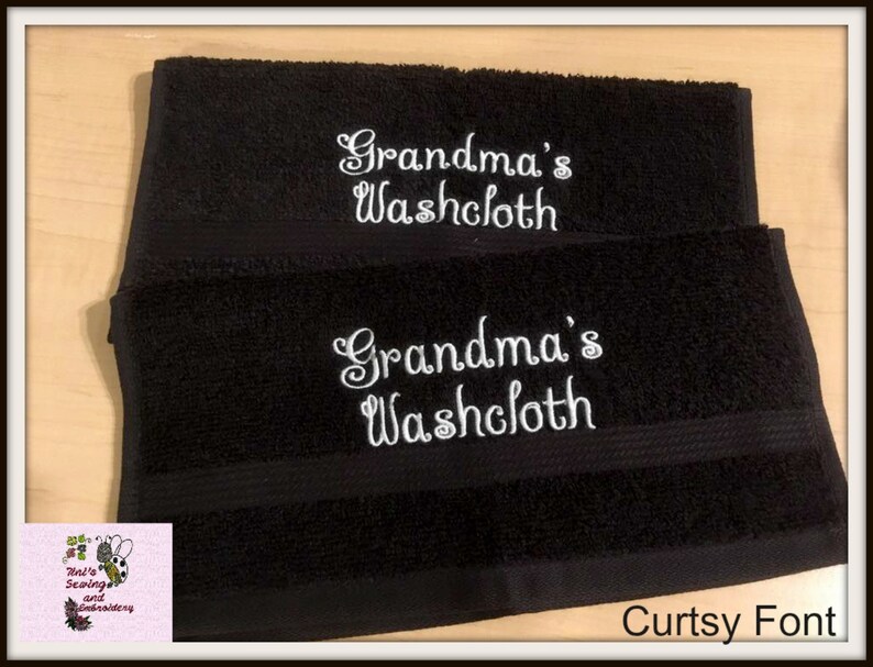 Może przedstawiać: Dwa czarne ręczniki do twarzy z białym haftem, na kt&oacute;rym widnieje napis "Grandma's Washcloth" w ozdobnym, pochylonym kroju pisma. Pod ręcznikami widoczny jest napis "Curtsy Font".