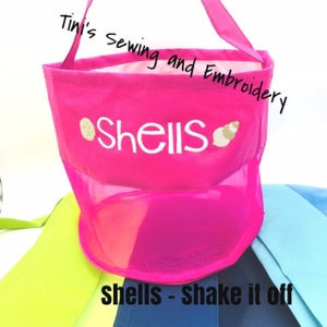 May include: Pink mesh beach bag with a white embroidered design that says "Shells" and a small gold shell graphic. The bag has a pink fabric handle and the text "Shells - Shake it off" is printed below the bag.