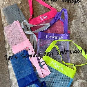 May include: A collection of mesh tote bags in various colors, including pink, purple, blue, and green. Each bag has a contrasting colored handle and the names "Ella", "Lorena", and "Mack" embroidered on them. The text "New style Handle", "Tini's sewing and Embroidery", and "Preschool Font" are also visible.