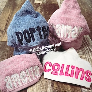 Puede incluir: Cuatro toallas con capucha en azul, rosa y blanco con nombres bordados que incluyen Porter, Palmer, Amelia y Collins. El texto @Tini's Sewing and Embroidery y tinialabini.etsy.com es visible. Las toallas tienen un acabado de tela suave y texturizada.